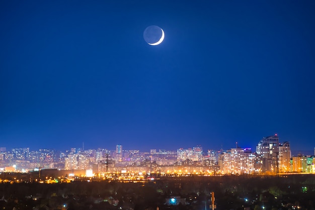 Ciudad de noche con luna nueva en el cielo azul oscuro con estrellas