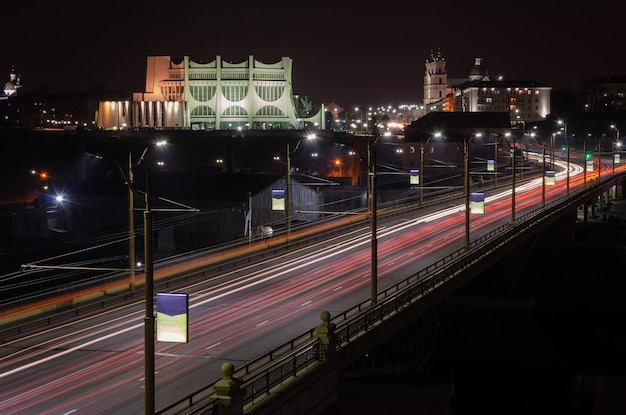 Ciudad nocturna Los senderos de luz en la calle Foto con velocidad de obturación lenta Un largo puente que cruza el río conduce a la gran ciudad Una autopista concurrida en el centro de la ciudad