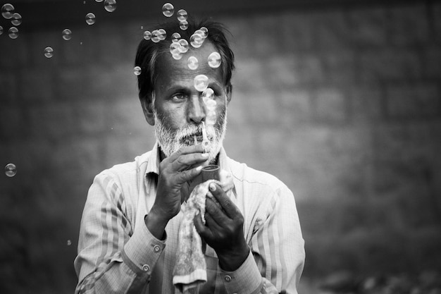 Un ciudadano indio de la tercera edad jugando con burbujas al aire libre en blanco y negro