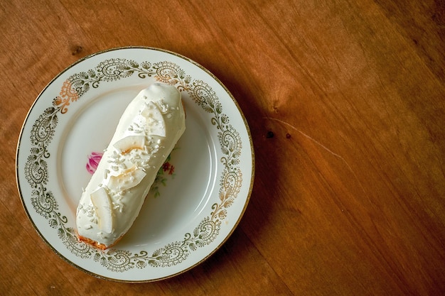 Éclair de coco com cobertura branca em um prato branco sobre um fundo de madeira