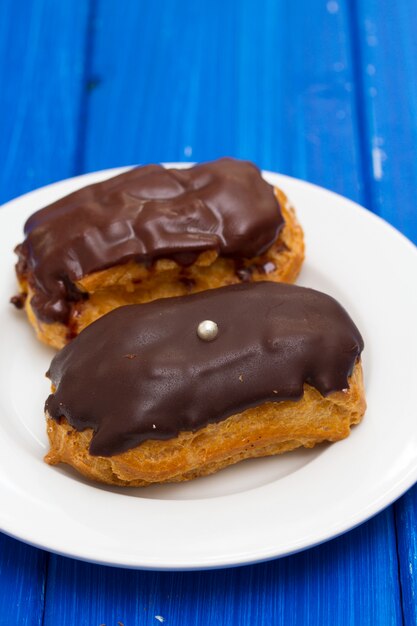 Éclairs de chocolate no prato branco na superfície de madeira