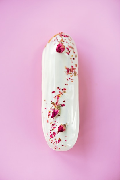 Éclairs ou profiteroles com esmalte de chocolate branco com sabor rosa sobre fundo rosa.