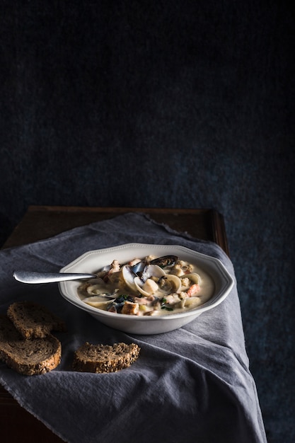 Clam chowder em um prato branco. Os principais ingredientes são mariscos, caldo, manteiga, batata e cebola.