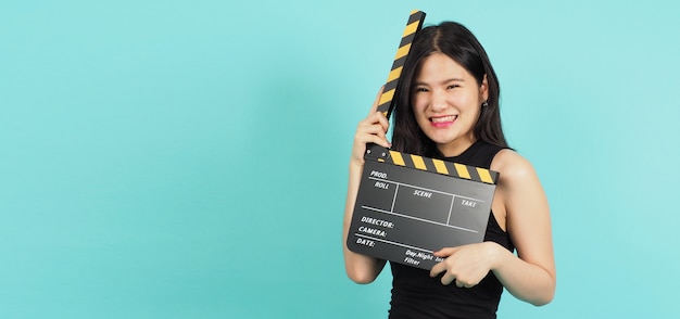 Clapper Board oder Film Clapperboard in Teenager-Mädchen- oder Frauenhand mit schwarzer und gelber Farbe. Es wird in der Videoproduktion, Film-, Kinoindustrie auf grünem oder Tiffany Blue-Hintergrund verwendet. Sie trägt ein schwarzes Kleid