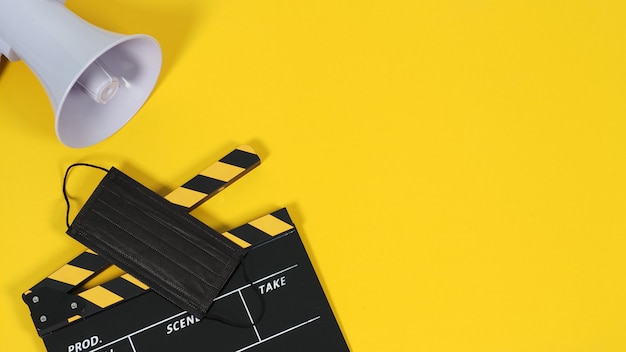 Clapper Board oder Filmschiefer und schwarzes Gesichtsmasken-Megaphon auf gelbem Hintergrund. Gelbe und schwarze Farbe.