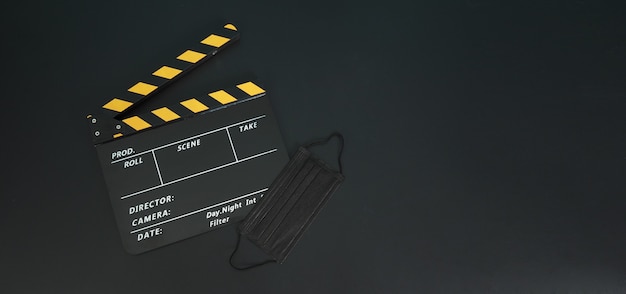 Claqueta amarilla o pizarra de película con mascarilla negra o máscara médica aislada. Se utiliza en el cine, la producción de películas y la industria del cine sobre fondo negro.Covid-19 o concepto de distancia social.