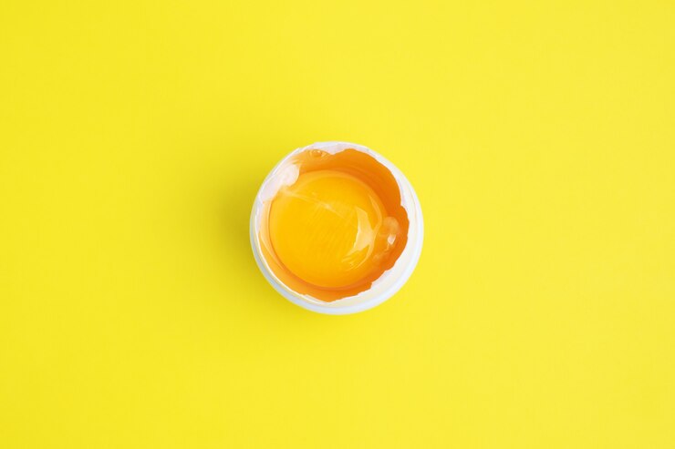 Clara de huevo de gallina cruda y yema en media cáscara en amarillo