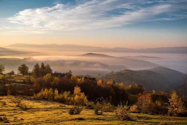 Clareira verde do amanhecer em um fundo de montanhas no nevoeiro o céu brilha com belas cores Temporada de outono