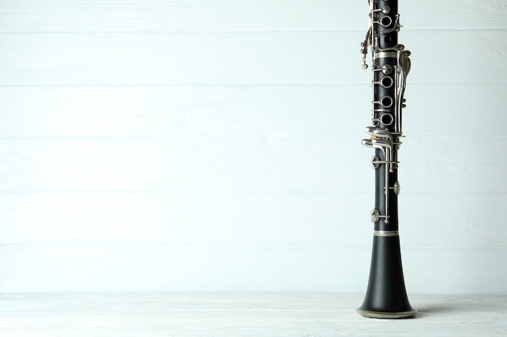 Foto clarinete em fundo branco de madeira, espaço para texto.