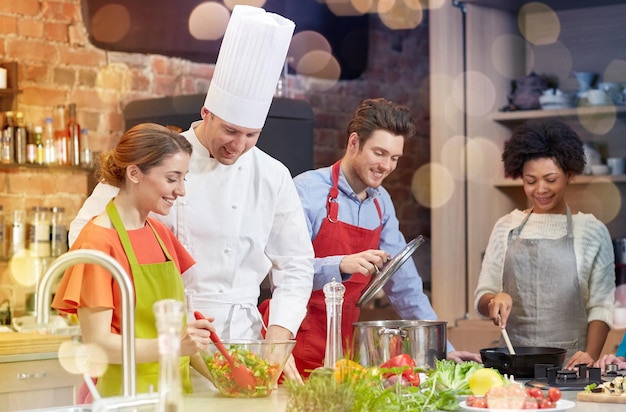 clase de cocina comida culinaria y conceptos de personas grupo feliz de amigos y chef masculino cocinero cocinando en la cocina