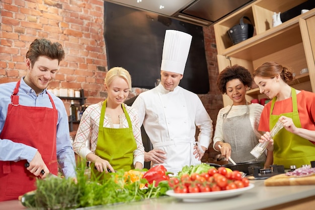 clase de cocina, concepto culinario, de comida y de personas - feliz grupo de amigos con chef masculino cocinando en la cocina