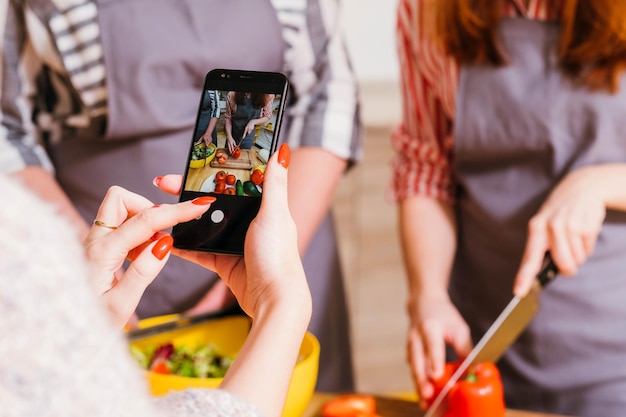 Clase de cocina en línea Asistente femenina filmando mujeres preparando ensalada de verduras Fondo borroso