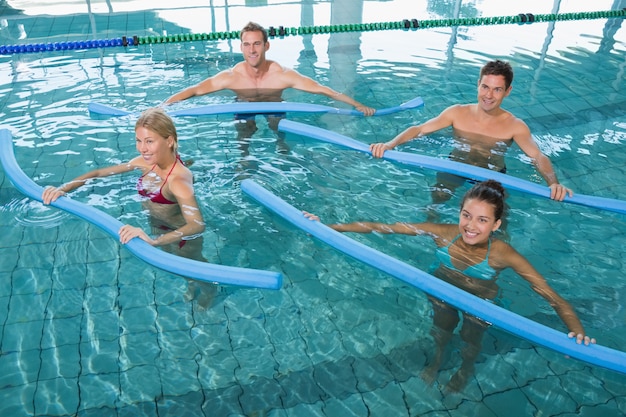 Foto clase de fitness feliz haciendo aeróbic acuático con rodillos de espuma