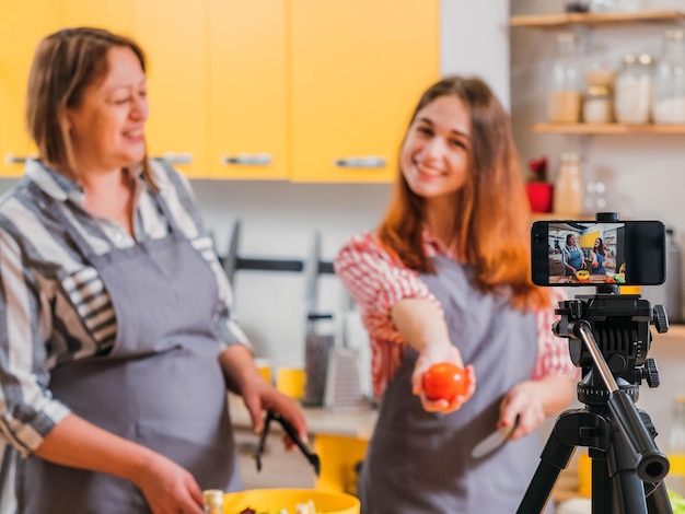 Clase en línea de dieta saludable Madre e hija grabando video preparando ensalada con verduras orgánicas Fondo borroso