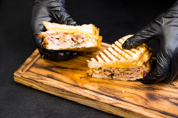 Clase magistral culinaria. Primer plano de las manos del chef sosteniendo una mitad de sándwich de cerdo desmenuzado con queso sobre tabla de madera.