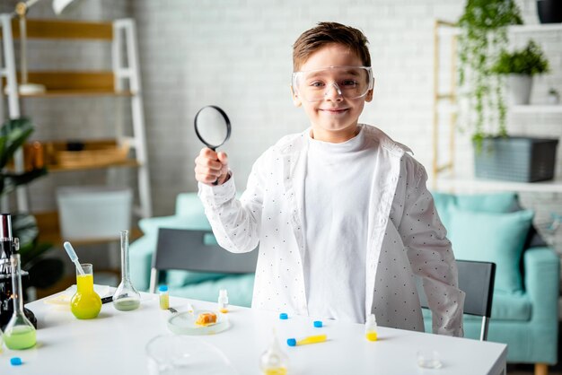 En la clase de química, un niño sonriente sosteniendo una lupa