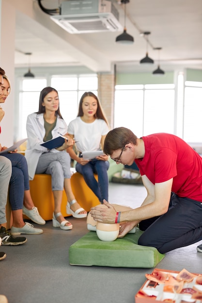 Clase de reanimación cardiopulmonar con instructores jóvenes caucásicos hablando y demostrando ayuda de primeros auxilios