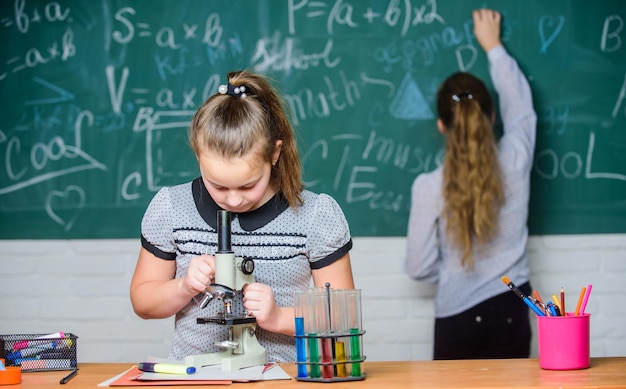 Clases de química Experimento educativo Niñas compañeras de clase estudian química Microscopio tubos de ensayo reacciones químicas Alumnos en pizarra lección de química Práctica de laboratorio Ciencia fascinante