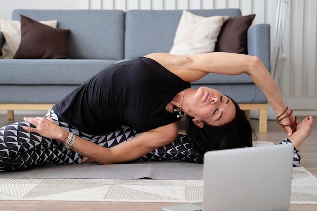 Clases de yoga Una mujer delgada en un chándal se sienta en una pose de yoga frente a una computadora portátil Primer plano