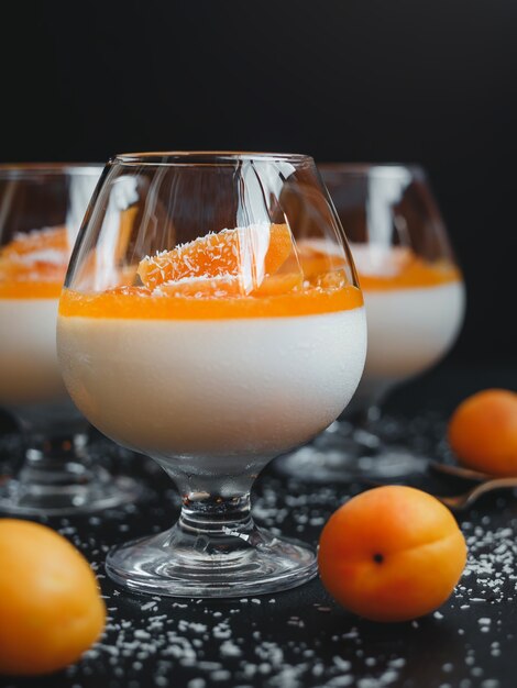 clásica panna cotta de vainilla en un vaso con albaricoques y hojuelas de coco