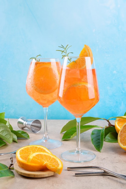 Clásico aperitivo italiano aperol spritz cóctel en dos vasos con hielo naranja sobre fondo azul en el podio de mármol