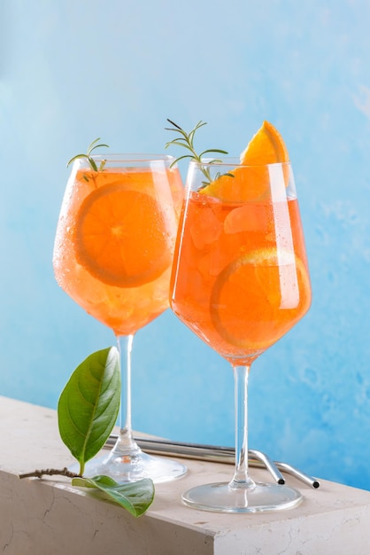 Foto clásico aperitivo italiano aperol spritz cóctel en dos vasos con hielo naranja sobre fondo azul en