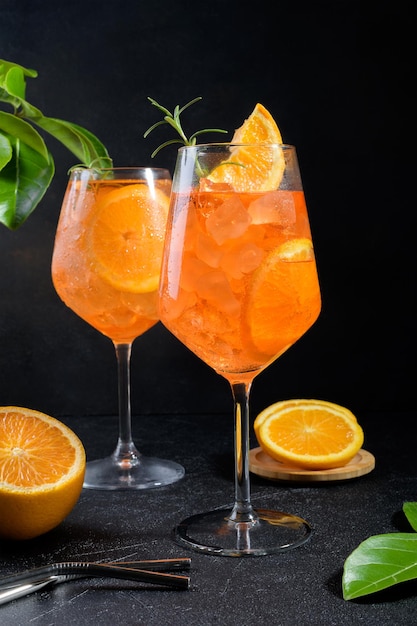 Clásico aperitivo italiano aperol spritz cóctel en dos vasos con una rodaja de hielo de naranja sobre fondo negro