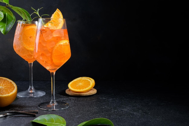 Clásico aperitivo italiano aperol spritz cóctel en dos vasos con una rodaja de hielo de naranja sobre fondo negro