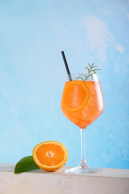 Clásico aperitivo italiano aperol spritz cóctel en vaso con hielo y rodaja de naranja sobre azul claro