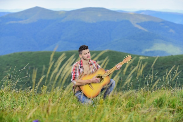 Clásico Cool guitarrista acústico canción de música country hombre sexy con guitarra en camisa a cuadros moda hipster camping occidental y senderismo hombre vaquero feliz y libre tocar la guitarra al aire libre