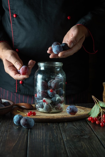 La clasificación de las ciruelas por las manos del cocinero La cocción de mermelada dulce de ciruelas frescas y azúcar en la mesa de la cocina El proceso de preservación de Prunus en un frasco