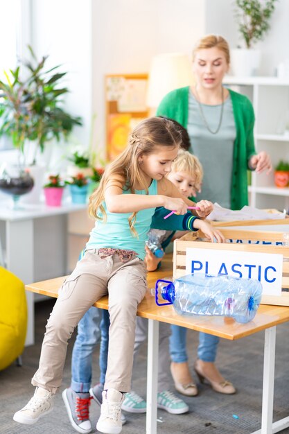 Clasificación de plástico. Hermosa niña sentada en la mesa en la escuela y clasificación de plástico con su compañero y maestro