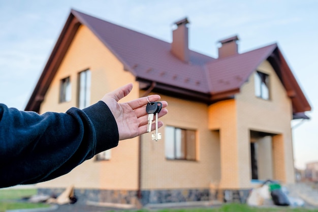 Clave en una mano frente a la casa Proyecto de construcción que se muda a una nueva hipoteca de alquiler y compra de bienes raíces