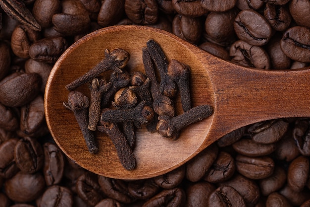 Clavo en una cuchara de madera con el telón de fondo de los granos de café