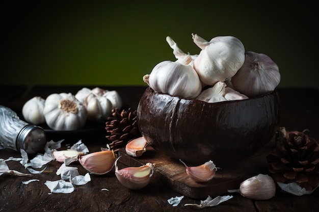 Los clavos de ajo y el bulbo del ajo por la mitad del cuenco de la cáscara del coco en la tabla de madera.