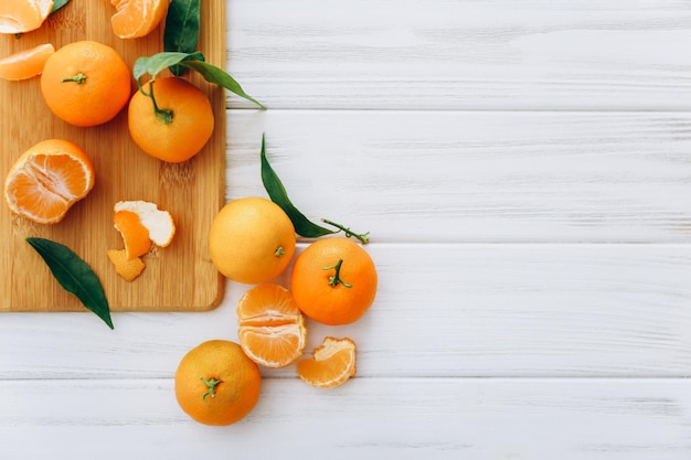 Clementinas frescas con hojas sobre mesa de madera blanca.