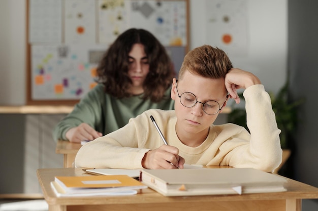 Cleverer jugendlicher Schüler, der sich während der Einzelaufgabe Notizen im Schreibheft macht