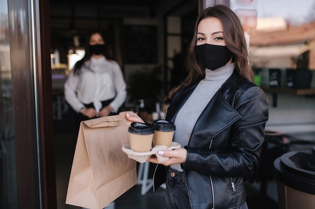 Clienta atractiva en mascarilla de pie al aire libre por café y comida para llevar y café