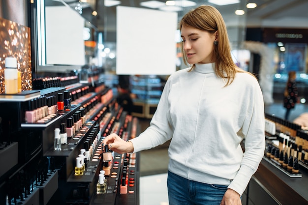 Clienta en busca de cosméticos en la tienda de maquillaje. Elegir esmalte de uñas en tienda de belleza, salón de maquillaje