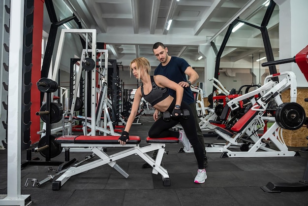 Una clienta en forma que trabaja con un instructor masculino personal con pesas pesadas en el deporte del gimnasio para un estilo de vida saludable