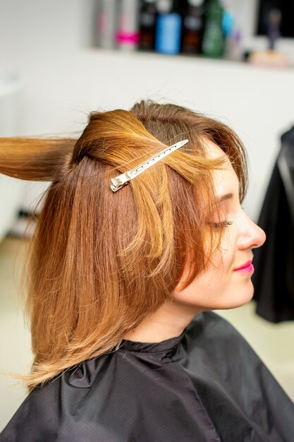 La clienta recibiendo un corte de pelo en el salón de belleza, joven disfrutando de un nuevo peinado.