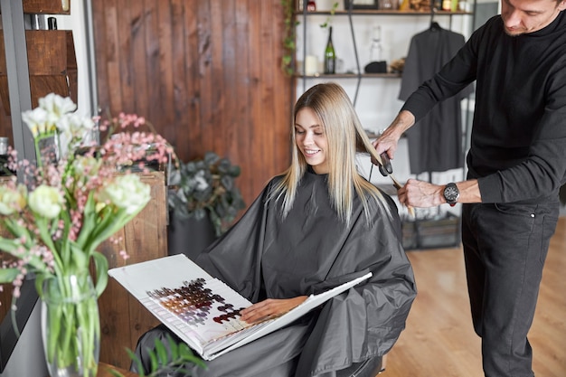 Clienta rubia está eligiendo el color en el libro mientras la peluquera se corta el cabello