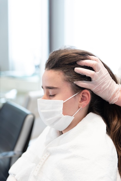 Un cliente adolescente con una máscara facial recibiendo un masaje capilar en un salón de belleza