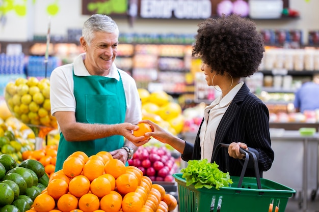 Foto cliente africano com verdureiro, segurando frutas laranja.