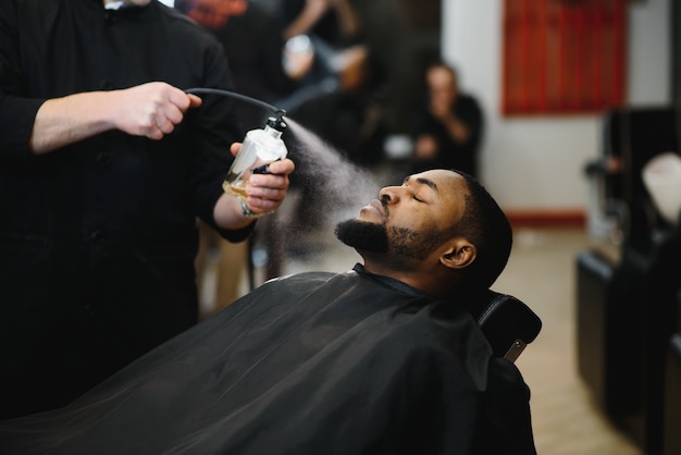 Cliente africano do sexo masculino cortando o cabelo na barbearia de cabeleireiro profissional