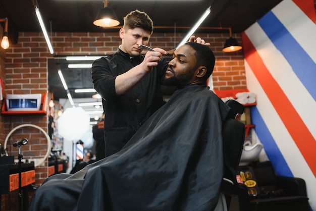 Cliente africano do sexo masculino cortando o cabelo na barbearia de cabeleireiro profissional