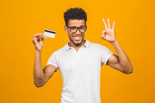 Cliente afroamericano hombre sujetando una tarjeta de crédito sobre fondo amarillo aislado