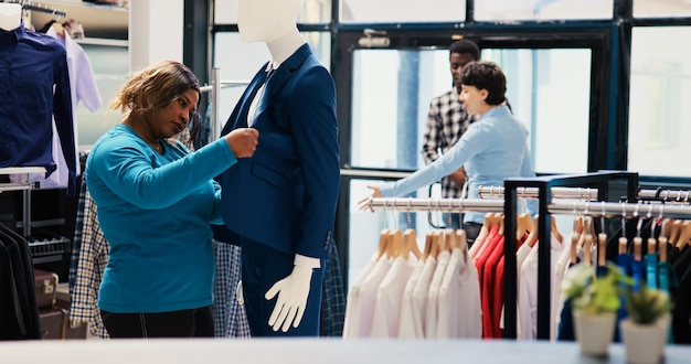 Cliente afroamericano mirando un traje elegante, analizando la tela de la mercancía en una boutique moderna. Mujer adicta a las compras de ropa de moda, comprando artículos de moda en una tienda de ropa