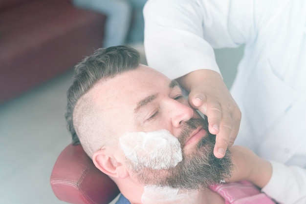 Cliente com espuma no rosto durante o barbear de barba na barbearia Toned