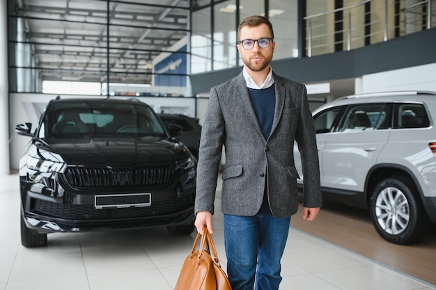 Cliente comprador masculino de terno, escolha o automóvel para ir olhar para o lado, quer comprar automóvel novo no showroom do carro, salão da concessionária, loja do salão do automóvel, conceito de vendas interno